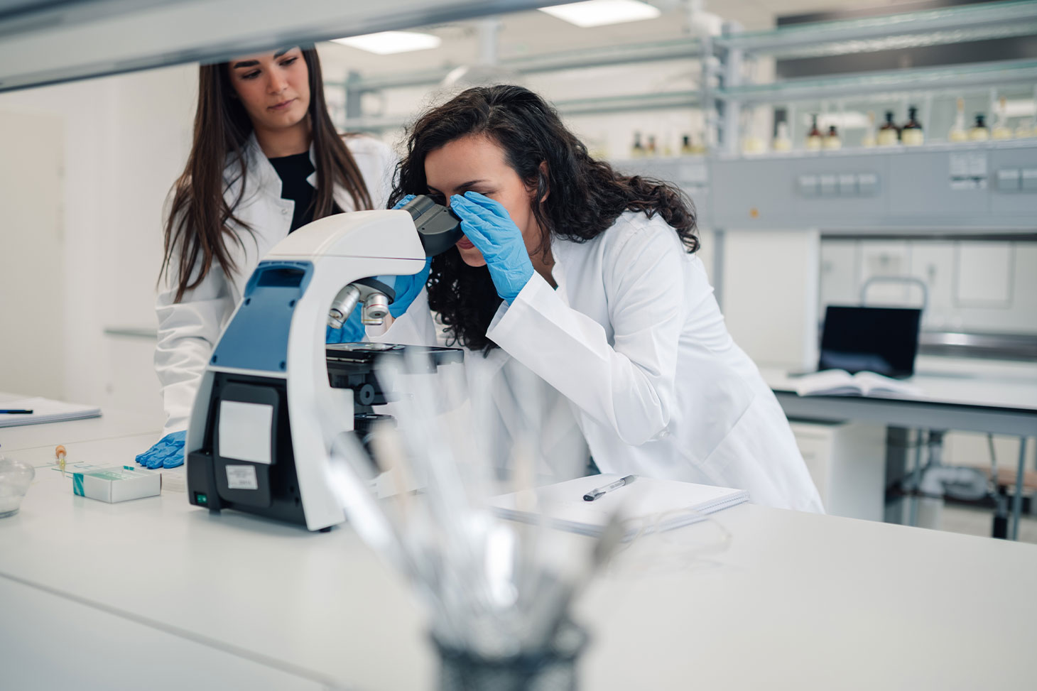 Deux jeunes chercheuses en blouse blanche devant un microscope dans un laboratoire